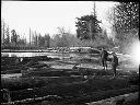 Two men on logs at log pond, circa 1920, #G0630_1