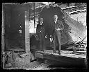 Two men in sawmill interior on log carriage near bandsaw, circa 1907, #G0974_1